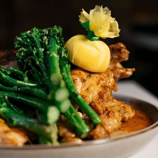 Italian chicken dish with broccolini and a lemon wrapped in yellow mesh, served in a bowl.